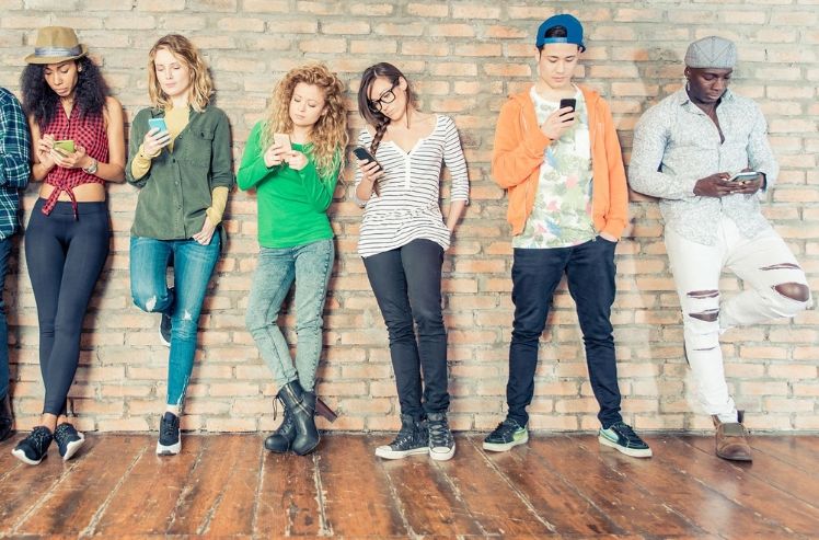 Sechs junge Menschen stehen an der wand mit smartphone in der hand