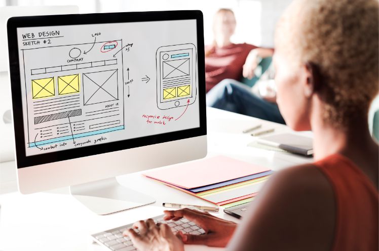 Frau sitzt an desktop und erstellt mockup fuer web design