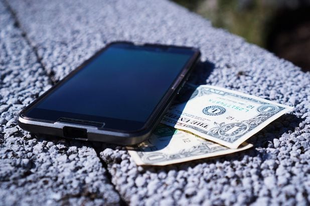 Smartphone liegt neben Geld auf einem Tisch