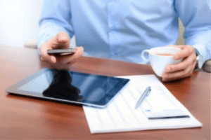man drinks his coffee in front of his tablet and some documents