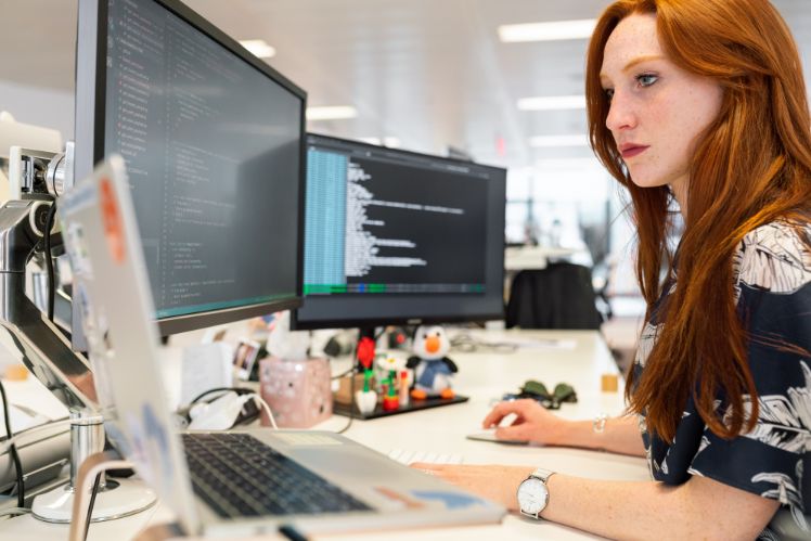 une femme travaillant sur 3 écrans,affichant differentes codes illustrant le principe d'automatisation intelligente des processus 