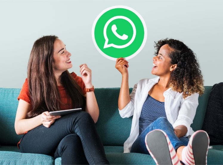 deux jeunes filles assises sur un sofa dans l'une tient le logo de l'application populaire whatsapp