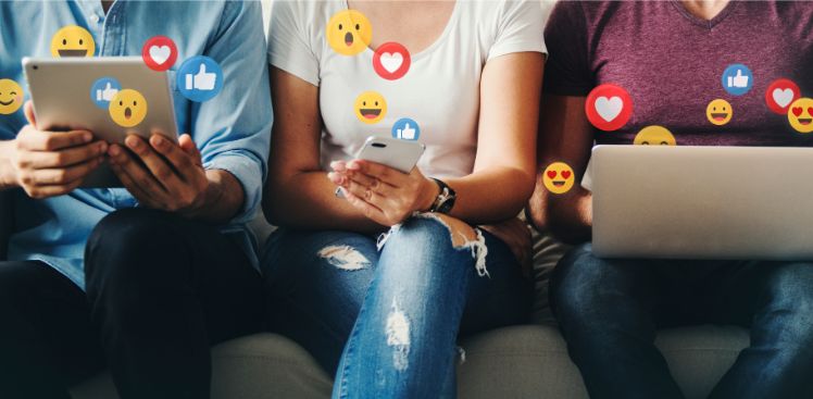 Application populaire : 3 personnes assises, une avec une tablette a la main, une autre avec son téléphone et la troisième avec un pc et différents emojis des applications populaires
