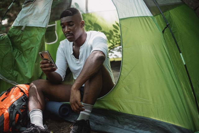 homme assis au bord d'une tente verte avec un téléphone dans la main